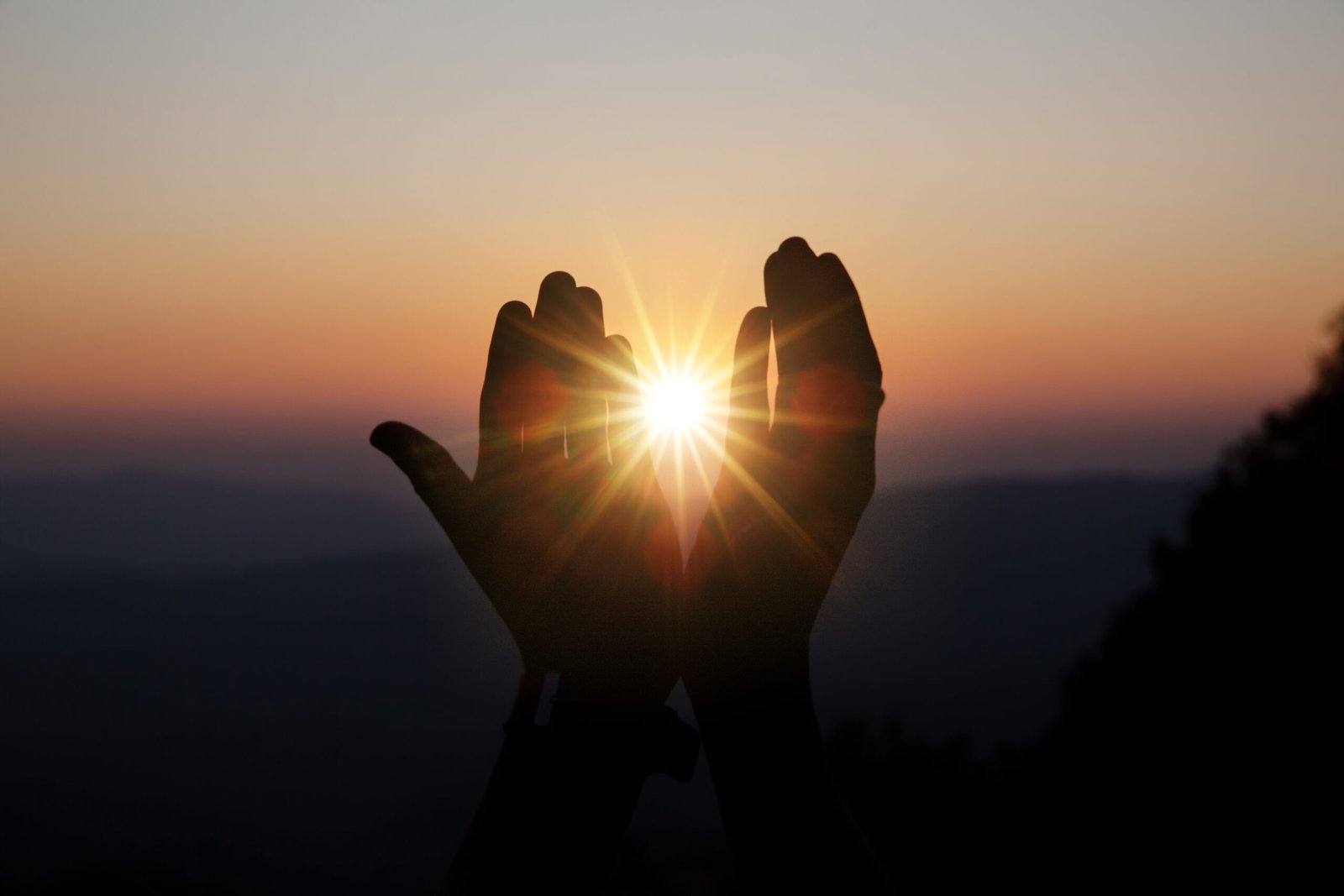 Hands held up in prayer against the setting sun